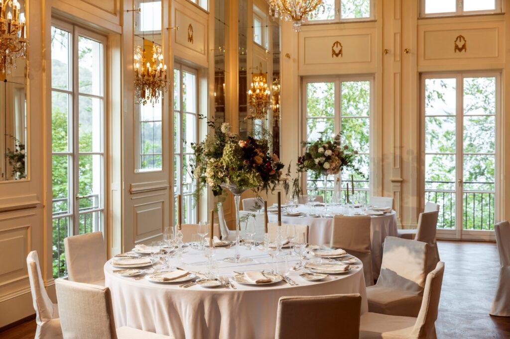 Hochzeitslocation Rosewood Schloss Fuschl: runde Hochzeitstafeln mit Blumen im lichtdurchfluteten Ballsaal