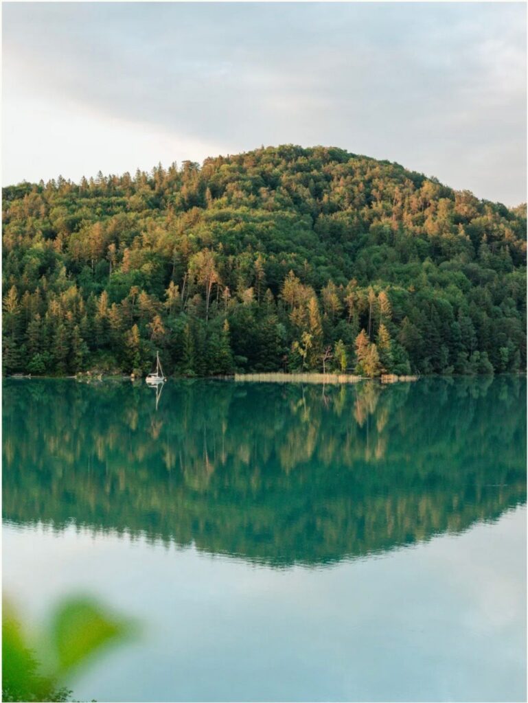 Bewaldeter Hügel spiegelt sich im ruhigen, türkisblauen Wasser des Fuschlsees im Salzkammergut