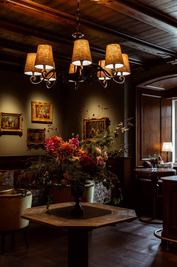 Grüner Salon mit dunkler Holzdecke, Lampen und großem Blumenarrangement für kleine Empfänge im Schloss