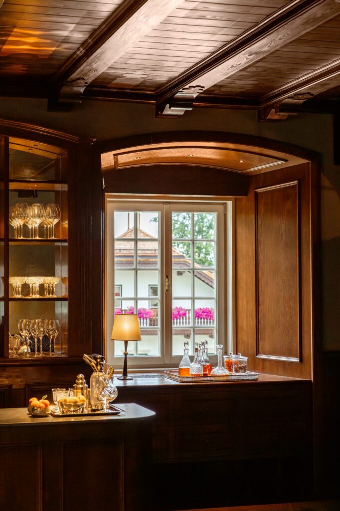 Holzvertäfelter Raum mit Vitrine, Gläsern und Fensterblick im Grünen Salon des Rosewood Schloss Fuschl