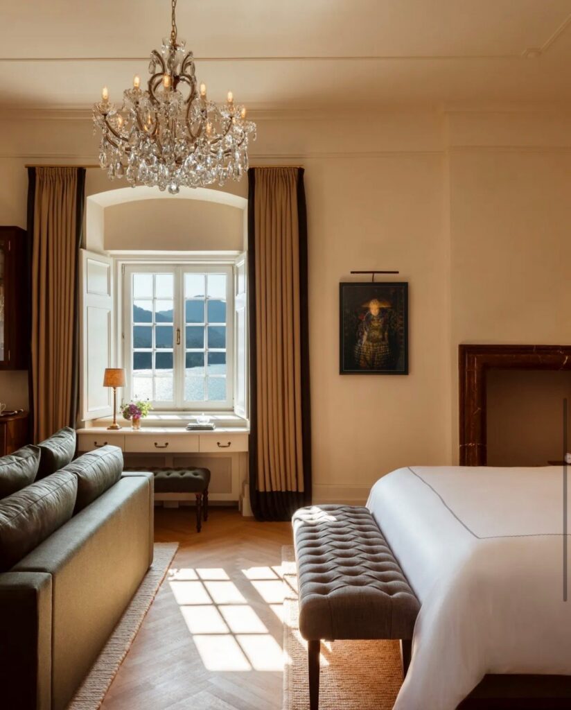 Helles Hotelzimmer mit Kronleuchter, Doppelbett und Sitzbank für Hochzeitsgäste im Schloss am See