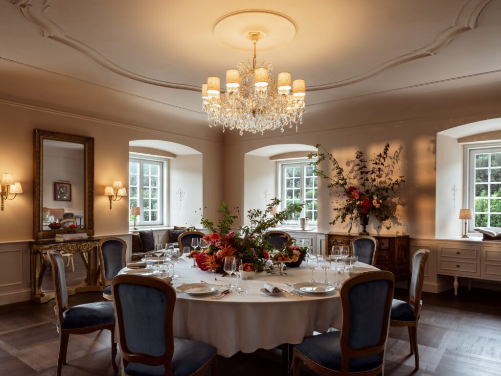 Runde, festlich eingedeckte Tafel mit Blumen unter einem Kronleuchter im Rosa Salon des Schlosses