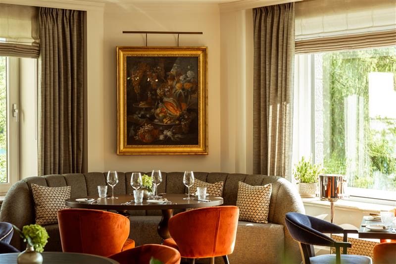 Salon mit historischem Gemälde, orangefarbenen Sesseln und Fensterfront im Rosewood Schloss Fuschl